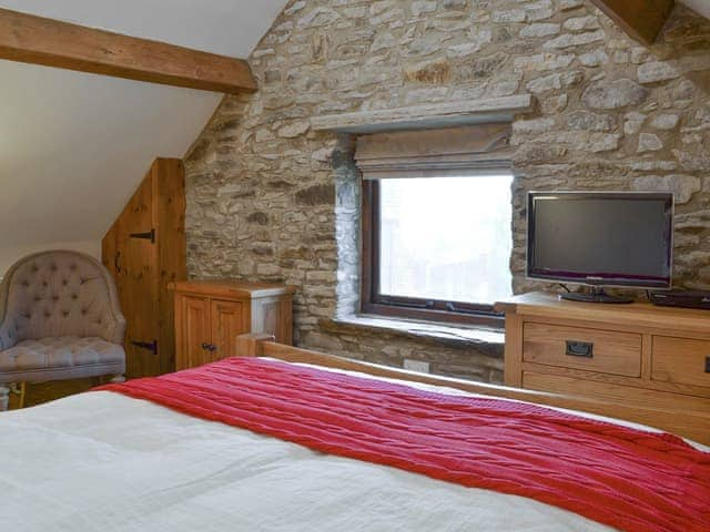 Double bedroom with exposed wooden beams and feature stone wall | The Old Stable, Barber Booth, near Edale