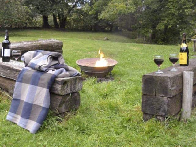 Fire-pit area with rustic seating within the gardens | Ringslade Barn and Cinema, Highweek, near Newton Abbot