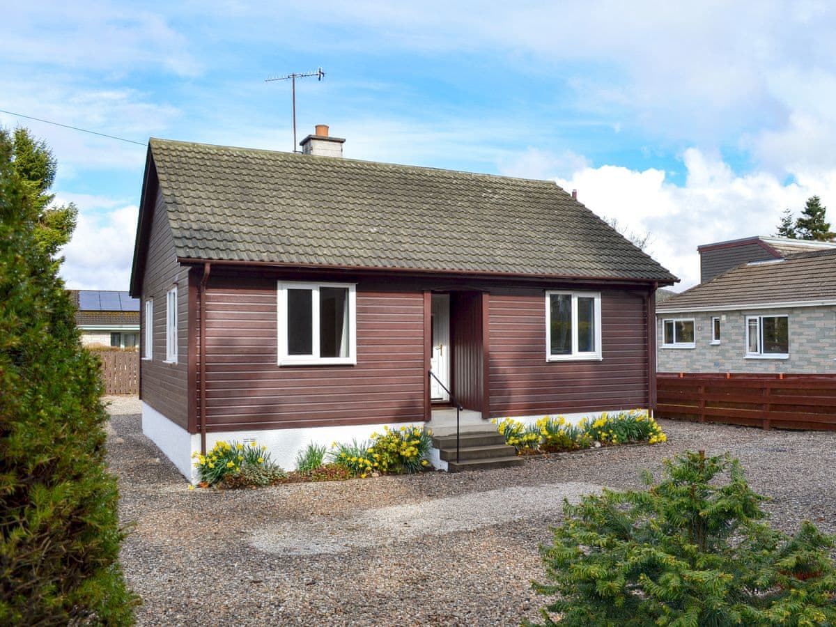 Brown timber-clad Cedar Cottage with a gravel garden and entrance steps in Grantown-on-Spey