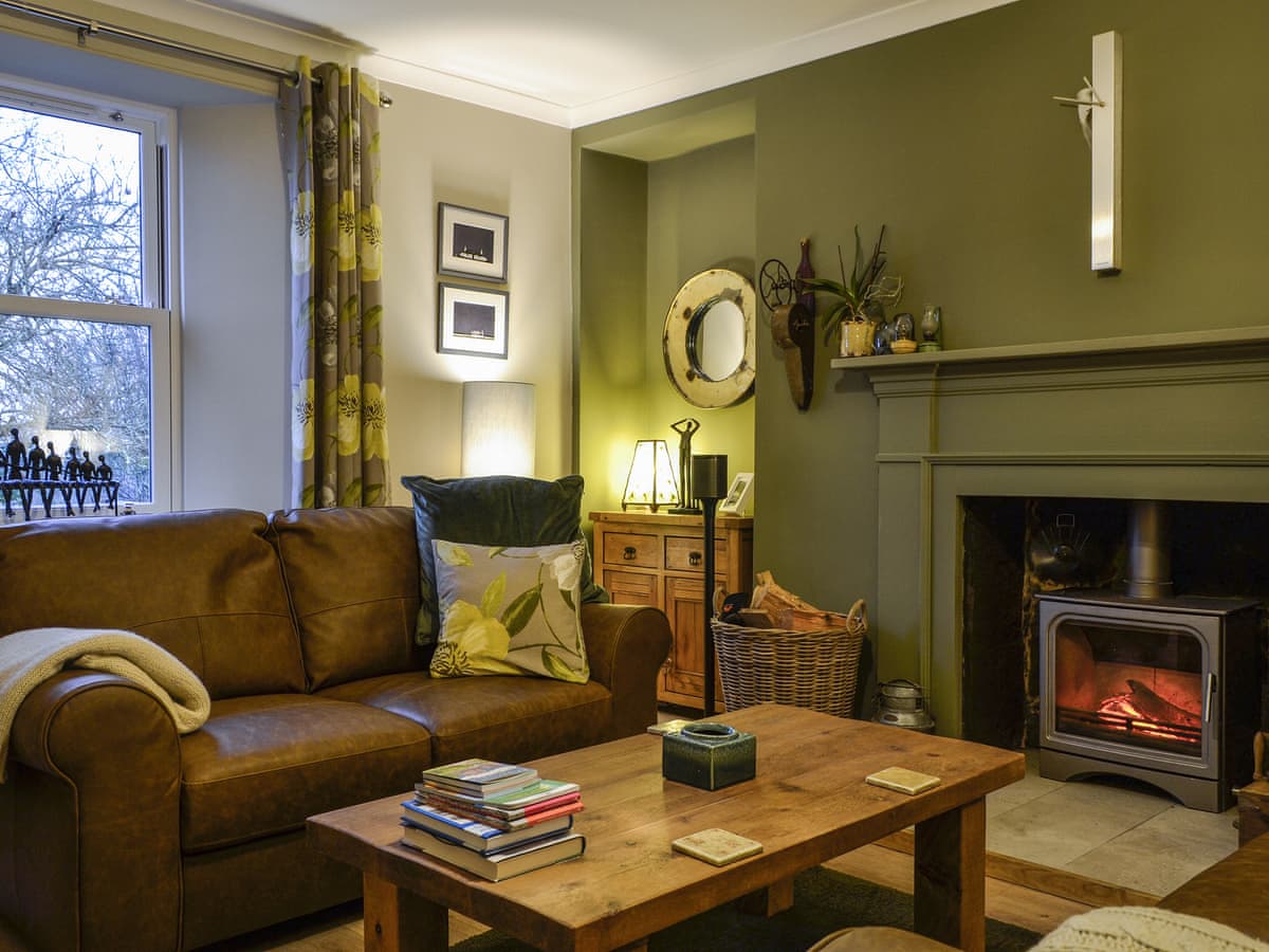 Cotlea East Cottage sitting room with a leather sofa, wooden coffee table and lit wood burner