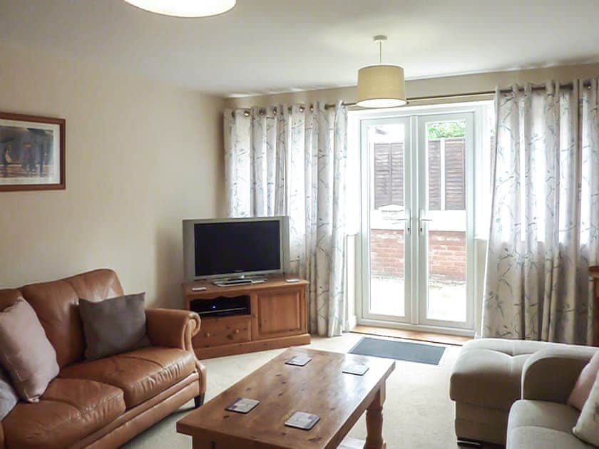 Cosy living room with French doors leading to garden | Old Dairy Court, Sheringham