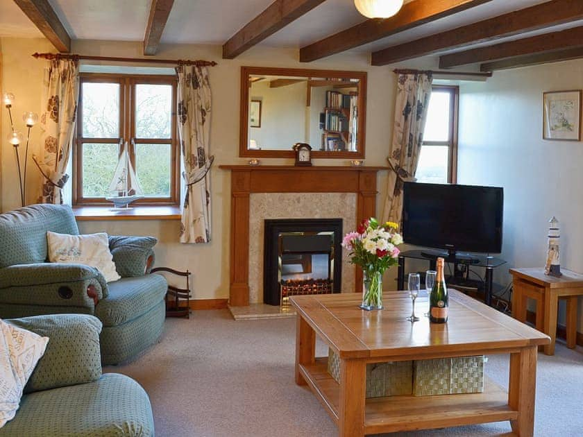 The living room features exposed beams and an electric coal effect fire | Coachmans Cottage, White Cross, near Newquay