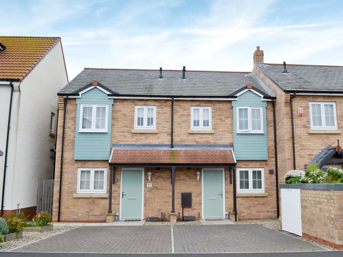 Sea Breeze cottage frontage with pale blue doors and cladding above a paved parking area in Beadnell