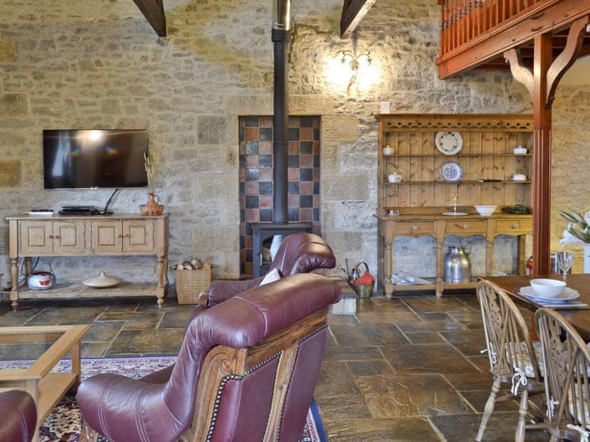 Open-plan living space with exposed stone feature wall and a wood burning stove | The Dairy, Biggin by Hartington, near Buxton