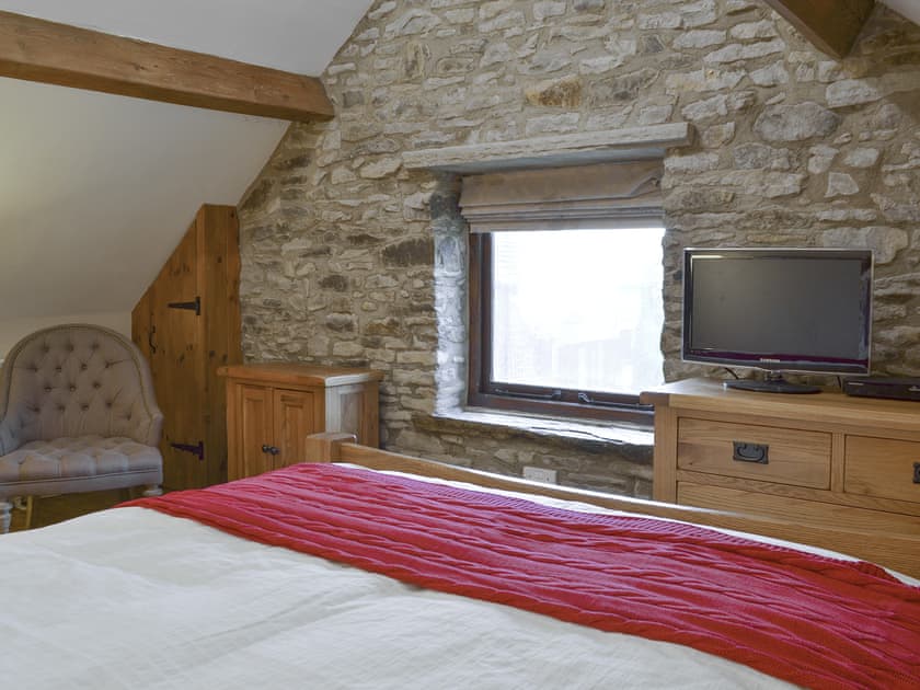 Double bedroom with exposed wooden beams and feature stone wall | The Old Stable, Barber Booth, near Edale