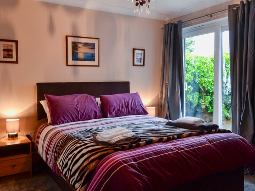 Bedroom with kingsize bed, patio doors leading to patio and en-suite | Ivy Cottage, Montrose