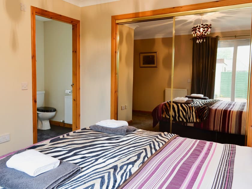 Bedroom with kingsize bed, patio doors leading to patio and en-suite | Ivy Cottage, Montrose