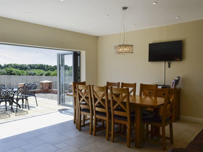 Dining room/kitchen with breakfast bar, TV, tiled floor and bi-fold doors to patio | Birchfield, Rhuallt, near St Asaph