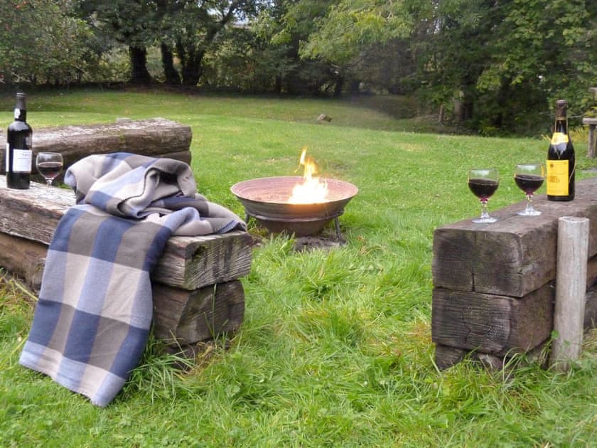 Fire-pit area with rustic seating within the gardens | Ringslade Barn and Cinema, Highweek, near Newton Abbot